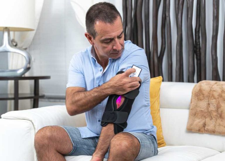 Person pressing button on controller attached to OnLux Elbow Pad on elbow.